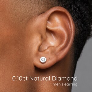 May include: A silver-toned stud earring featuring a round, bezel-set 0.10ct natural diamond. The text 0.10ct Natural Diamond is printed in white at the bottom of the image, along with the text men's earring below it.