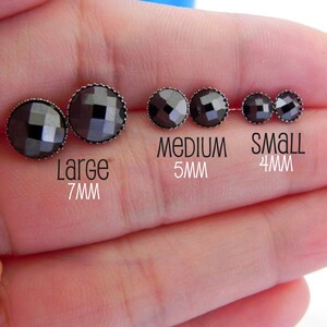 May include: Four black gemstone earrings in different sizes. The earrings are 7mm, 5mm, and 4mm in diameter. The earrings are on a hand.