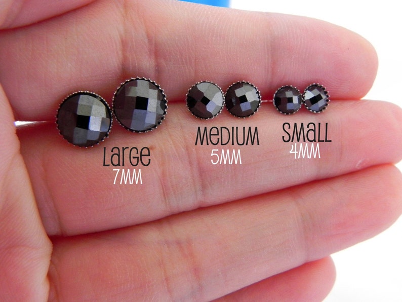 May include: Four black gemstone earrings in different sizes. The earrings are 7mm, 5mm, and 4mm in diameter. The earrings are on a hand.