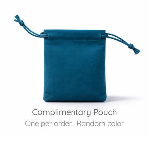Puede incluir: Una bolsa con cord&oacute;n de terciopelo color verde azulado con cordones a juego anudados en los extremos. El texto debajo de la bolsa dice: Complimentary Pouch. One per order &middot; Random color. La bolsa es rectangular con fondo plano y parte superior fruncida.