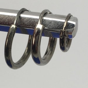 May include: Three silver hoop earrings of different sizes, hanging on a metal rod.