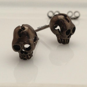 Op de afbeelding: Een paar zilveren schedel oorbel studs. De schedels zijn gedetailleerd en hebben een licht verweerde afwerking.