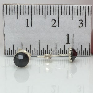 May include: A pair of silver stud earrings with black and red gemstones. The earrings are about 1/2 inch in diameter.