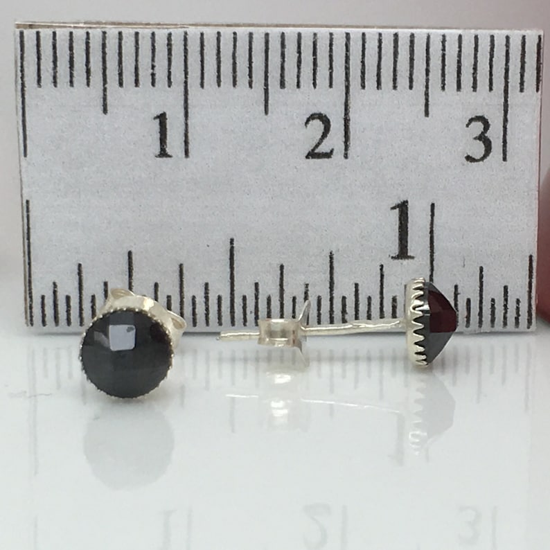 May include: A pair of silver stud earrings with black and red gemstones. The earrings are about 1/2 inch in diameter.