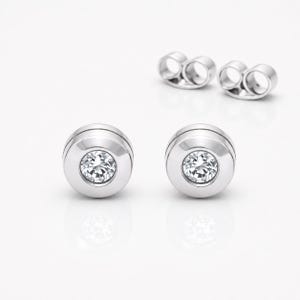 May include: A pair of silver-toned stud earrings featuring a circular bezel setting that holds a single clear, round-cut gemstone in the center. The earrings include matching silver-toned butterfly-style earring backs positioned behind them.