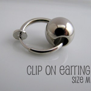 Może przedstawiać: Srebrny kolczyk na klipsie z okrągłą kulką. Kolczyk jest oznaczony "CLIP ON earring size M".