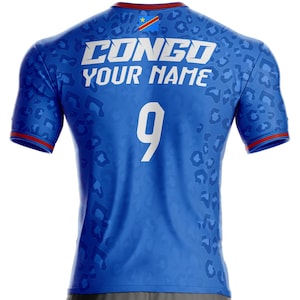 Op de afbeelding: Blauw shirt met het woord "CONGO" en "YOUR NAME" in het wit. Het nummer "9" staat ook in het wit. Het shirt heeft een luipaardprint en de vlag van de Democratische Republiek Congo op de rug.