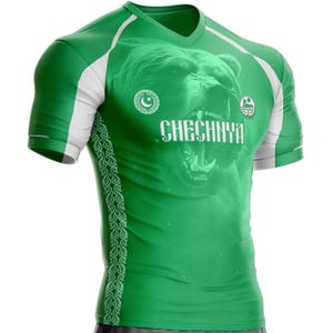 May include: Green athletic shirt with white accents and a V-neck. The shirt features a large bear graphic and the word "CHECHNYA" in white. Decorative patterns run down the sides. The shirt is designed for athletic activities.