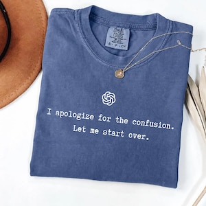 May include: A blue short-sleeved t-shirt featuring a white graphic of a circular logo and the text "I apologize for the confusion. Let me start over." The shirt has a crew neckline and a Comfort Colors brand label printed on the inside neck area.