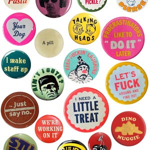 May include: A collection of colorful pinback buttons with various designs and text. The buttons feature phrases like "I love Pasta," "Talking Heads," and "I need a little treat." Other designs include a Frankenstein's monster, a clown, and a dinosaur.