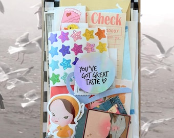 May include: A clear plastic bag filled with assorted stationery items including a sheet of holographic star stickers, a round sticker with the text YOU'VE GOT GREAT TASTE, a die-cut character sticker, a pink cake sticker, and a vintage-style check slip.