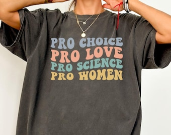 Op de afbeelding: Een donkergrijs T-shirt met de tekst "Pro Choice, Pro Love, Pro Science, Pro Women" in regenboogkleuren.
