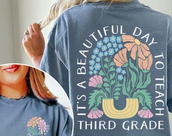 May include: Blue jean t-shirt featuring a floral design with the text "It's a beautiful day to teach Third Grade." The design includes orange, pink, and blue flowers in a yellow vase. A smaller version of the design is on the front.