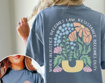May include: A blue jean t-shirt with a floral design and the text "When injustice becomes law, resistance becomes duty." The design features a rainbow-colored vase with flowers in shades of pink, blue, and green.