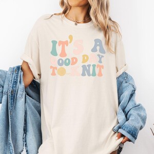 May include: A white t-shirt with the text "It's a good day to knit" in colorful, retro-style lettering.