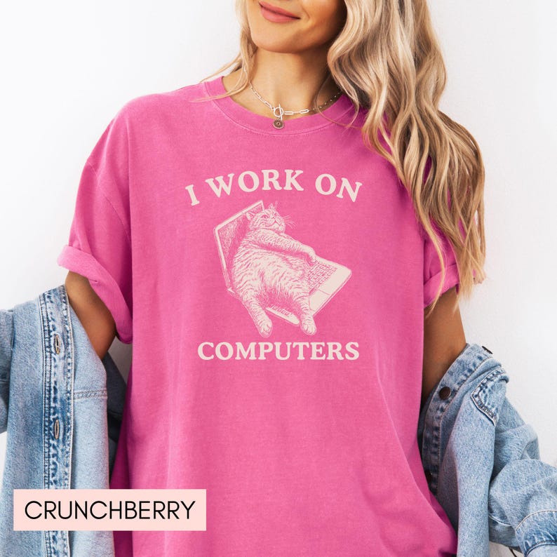Puede incluir: Una camiseta rosa con el texto "Trabajo en ordenadores" y una imagen de dibujos animados de un gato sentado en un port&aacute;til.