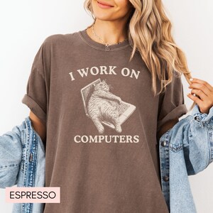 Puede incluir: Una camiseta marr&oacute;n con el texto "I work on computers" y un gato de dibujos animados sentado en un port&aacute;til. El gato es marr&oacute;n y blanco y tiene una expresi&oacute;n de sorpresa.