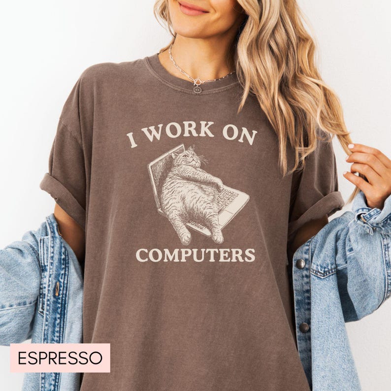 Puede incluir: Una camiseta marr&oacute;n con el texto "I work on computers" y un gato de dibujos animados sentado en un port&aacute;til. El gato es marr&oacute;n y blanco y tiene una expresi&oacute;n de sorpresa.