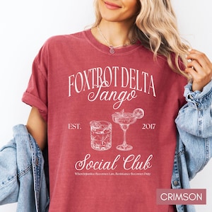 Op de afbeelding: Crimsonrode T-shirt met een wit grafisch ontwerp met de tekst "Fox Trot Delta Tango Social Club" met de data "EST. 2017" en de tekst "When Injustice Becomes Law, Resistance Becomes Duty".
