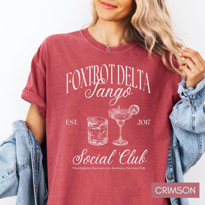 Op de afbeelding: Crimsonrode T-shirt met een wit grafisch ontwerp met de tekst "Fox Trot Delta Tango Social Club" met de data "EST. 2017" en de tekst "When Injustice Becomes Law, Resistance Becomes Duty".