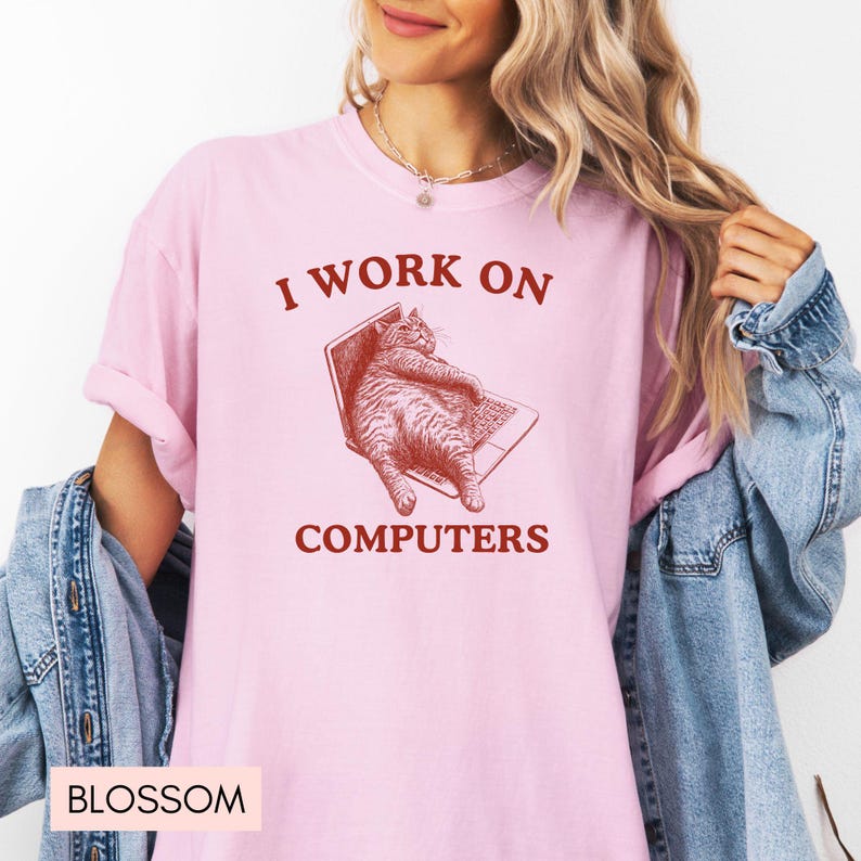 Puede incluir: Camiseta rosa con un gr&aacute;fico rojo de un gato sentado en un port&aacute;til. El texto "I work on computers" est&aacute; impreso en rojo debajo del gato.
