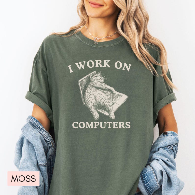 Puede incluir: Una camiseta verde con el texto "Trabajo en computadoras" y una imagen de dibujos animados de un gato sentado en una computadora port&aacute;til.