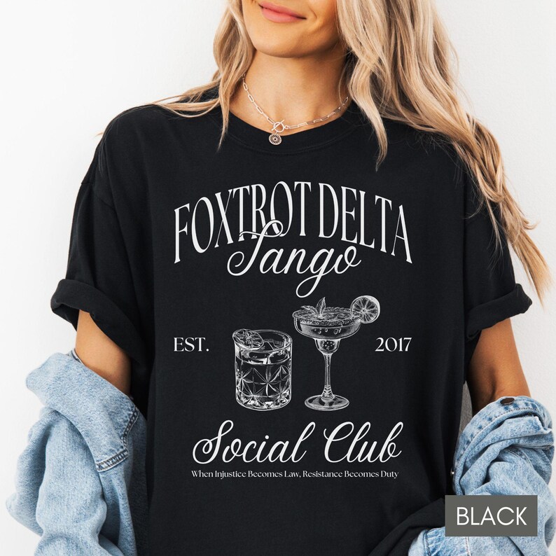 Op de afbeelding: Zwart T-shirt met witte tekst die "FOXTROT DELTA Jango EST. 2017 Social Club When Injustice Becomes Law, Resistance Becomes Duty" luidt. Het shirt heeft twee illustraties van cocktails.