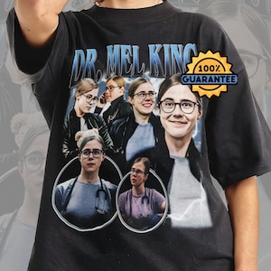 May include: Black t-shirt with a graphic of a person wearing glasses, and the text "DR. MEL KING" in blue. The design includes multiple images of the person and a "100% GUARANTEE" badge.