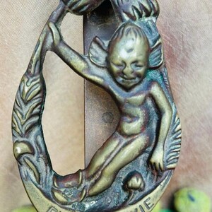 May include: A brass door knocker shaped like a pixie holding a leaf. The knocker is inscribed with the words "Exmoor Pixie".