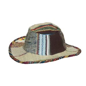 Op de afbeelding: Een patchwork hoed met een brede rand. De hoed heeft een mix van texturen en patronen, waaronder geweven stof, bruine panelen en kleurrijke geometrische ontwerpen. Het kleurenpalet van de hoed omvat beige, bruin en accenten van rood, blauw en groen.