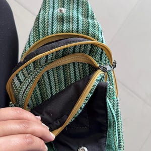 May include: Green and white striped sling bag with multiple zippered compartments. The bag has a black interior and gold-colored zippers. The bag is made of a woven fabric.