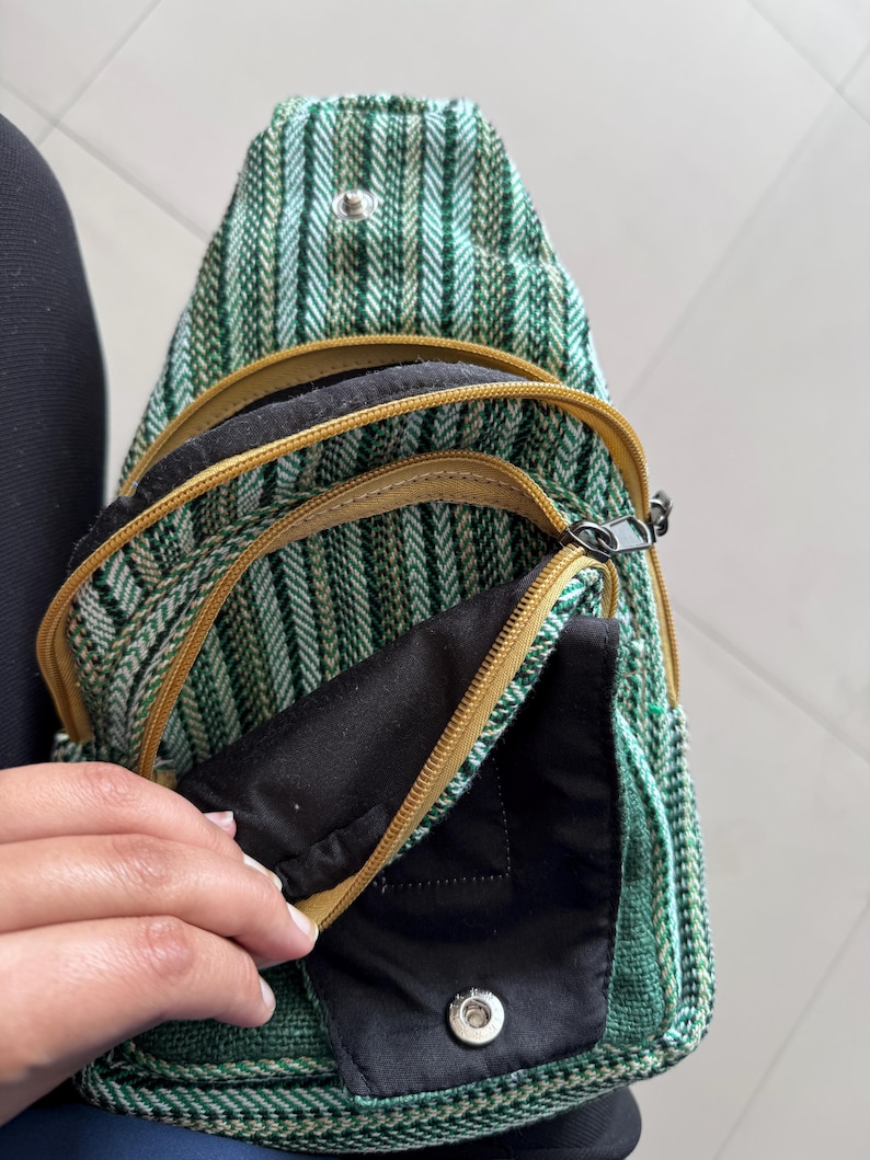 May include: Green and white striped sling bag with multiple zippered compartments. The bag has a black interior and gold-colored zippers. The bag is made of a woven fabric.