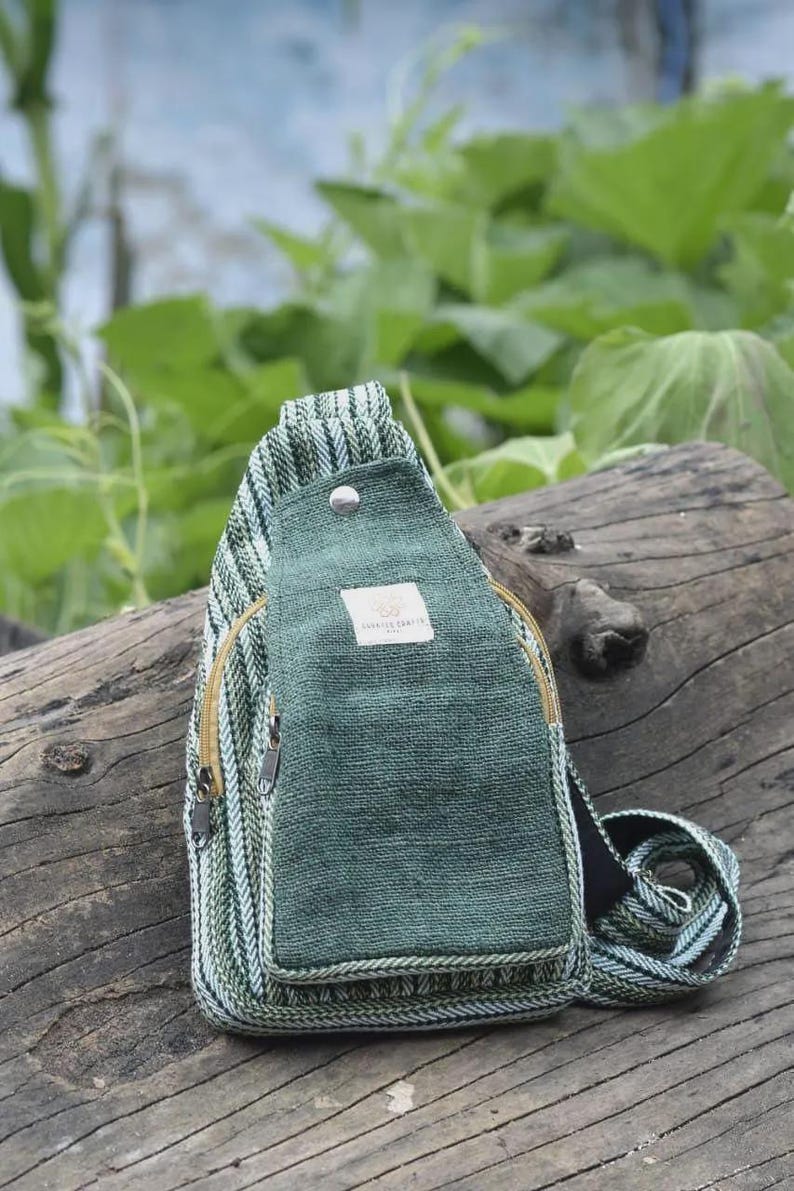 May include: Green and white striped sling bag with a solid green front pocket. The bag has a zipper closure and a small label. The strap is also green and white striped. The bag is made of a woven material.