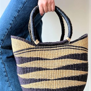 May include: Woven tote bag with a striped pattern in black, tan, and pink. The bag has a rounded top and black handles. The bottom of the bag has a stripe of pink and teal.