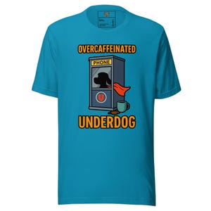 Pode incluir: Camiseta turquesa com um desenho animado. O desenho apresenta a silhueta de um cão numa cabine telefónica com uma capa vermelha, uma chávena de café e as palavras "OVERCAFFEINATED UNDERDOG" em amarelo e preto.