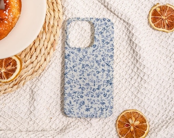 May include: A light blue phone case with a delicate floral pattern in a darker shade of blue. The case is rectangular with cutouts for the camera and buttons. The design features small flowers and leaves, creating a vintage aesthetic.