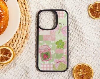 May include: A black phone case with a patchwork design featuring pink and green squares, a butterfly, a flower, a jar of jam, and a bow. The case has a black border and is surrounded by dried orange slices.