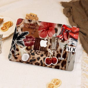 May include: A laptop skin featuring a collage of colourful images, including a red hibiscus flower, a coconut, a cherry, a martini glass, and a leopard print pattern. The skin also features the text "SAINT LAURENT" and "PANTONE 159".