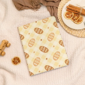 May include: A tablet case with a repeating pattern of bread loaves on a yellow and white checkered background. The case is rectangular and has rounded corners. The image also includes a wooden toy car, dried orange slices, and cinnamon sticks.