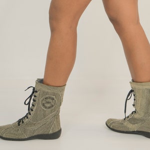 May include: A pair of grey canvas lace-up boots with black laces. The boots have a round toe and a thick black sole. The boots have a logo on the side that says "REBELCODE 1987"
