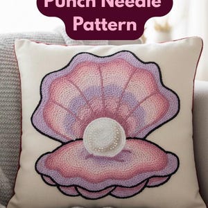 May include: Cream-colored decorative pillow featuring a punch needle pattern of a seashell with a pearl. The seashell design is in shades of pink and purple, outlined in black. The text "Punch Needle Pattern" is displayed at the top.