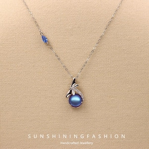 May include: A silver necklace with a blue pearl pendant. The pendant is surrounded by small clear stones and a dragonfly design. A small blue teardrop-shaped stone is set on the chain. The text "SUNSHININGFASHION" is at the bottom.
