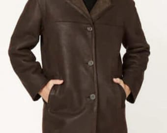 May include: A brown leather jacket with a shearling collar and three buttons. The jacket has two pockets and is worn over a black turtleneck. The person is smiling.