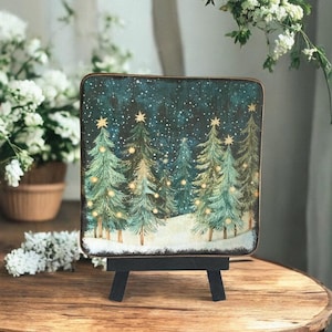 May include: A wooden Christmas-themed painting on a small black easel. The artwork depicts a snowy forest scene with illuminated Christmas trees under a starry night sky. The painting has a rustic, vintage aesthetic.