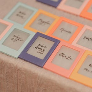 May include: A collection of colourful, framed place cards with handwritten names, including "Wai Kit", "Wai Hong", "Chin Li", and "Nicole".
