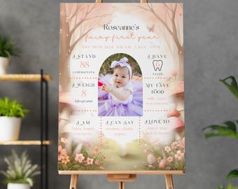 May include: A personalized fairy-themed first year sign on an easel. The sign features a photo of a baby girl in a purple tutu, with details including height (88 cm), weight (8 kg), and favorite things. The sign is decorated with a whimsical forest scene.