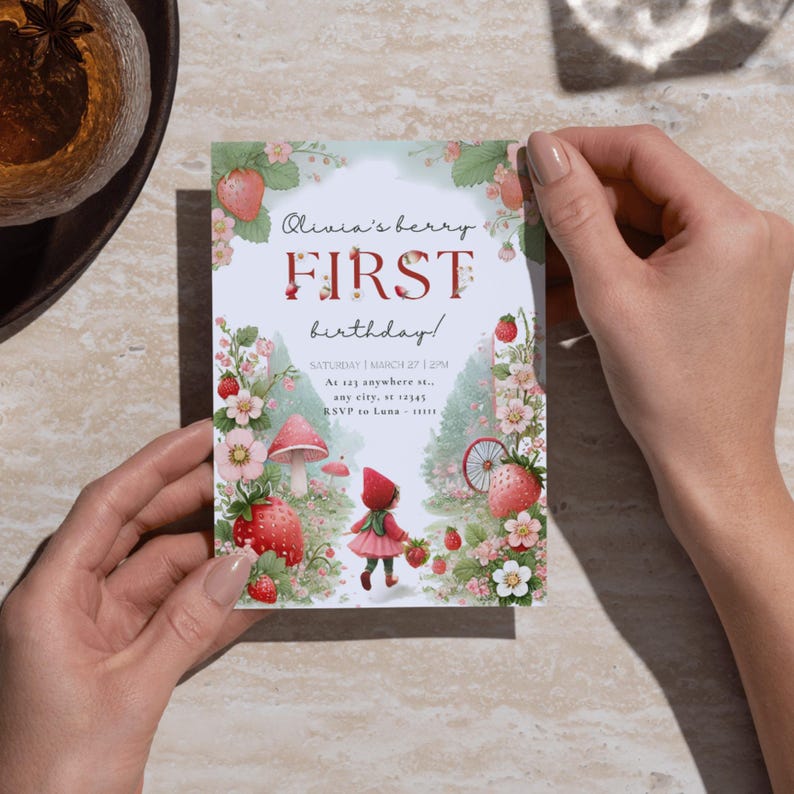 May include: A printable invitation for a first birthday party with a strawberry theme. The invitation features a girl in a red hooded dress walking through a strawberry patch with a mushroom and a bicycle in the background. The text on the invitation reads "Olivia's berry FIRST birthday!" and includes the date, time, and location of the party.