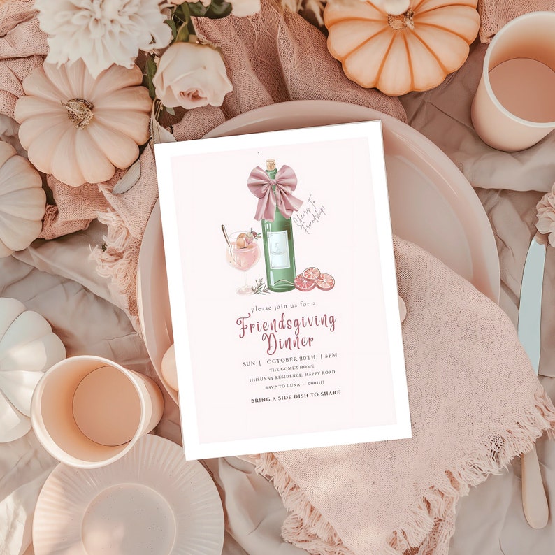 May include: A Friendsgiving Dinner invitation card with a watercolor illustration of a wine bottle, cocktail, and orange slices. The invitation is on a pink plate with a pink napkin, pumpkins, and flowers.