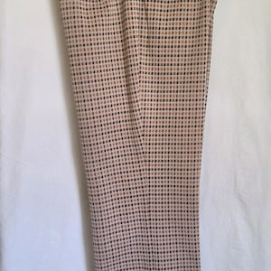 May include: Tan and black plaid trousers hanging on a white hanger. The pants have a classic, straight-leg cut and a subtle, repeating pattern of small squares in tan, black, and brown. The fabric appears to be a woven material.