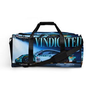 May include: A duffel bag featuring a graphic print of a teal race car with the number 80 and the text VINDICATED, SPA-FRANCORCHAMPS, and 24 HEURES DE SPA. The bag has black handles, a black shoulder strap, and a zippered top closure for storage.